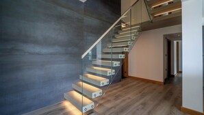 Een moderne trap met glazen balustrades en geïntegreerde verlichting, die naar een verdieping leidt.