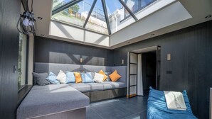 Een moderne woonkamer met een hoekbank, een blauwe relaxstoel en een dakraam.