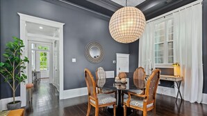 A dining room with a dark wood floor, a round table, and four chairs with woven seats. A large, round, woven light fixture hangs from the ceiling. - Uptown Designer Home l 3 bedroom l 3 blocks to Magazine St (New Orleans)