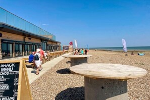 A beachside restaurant with outdoor seating, a visible menu board, and a clear view of the sea.