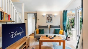 A living room with a flat-screen TV, a sofa, a coffee table, and a bookshelf. - Flint Cottage – 3 mins to beach (Littlehampton)