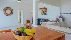 A spacious living area with a dining table, a ceiling fan, and a kitchen area with a gas stove and microwave. - Oceanfront Condo w/Pool & Balcony Views (Aguacate)