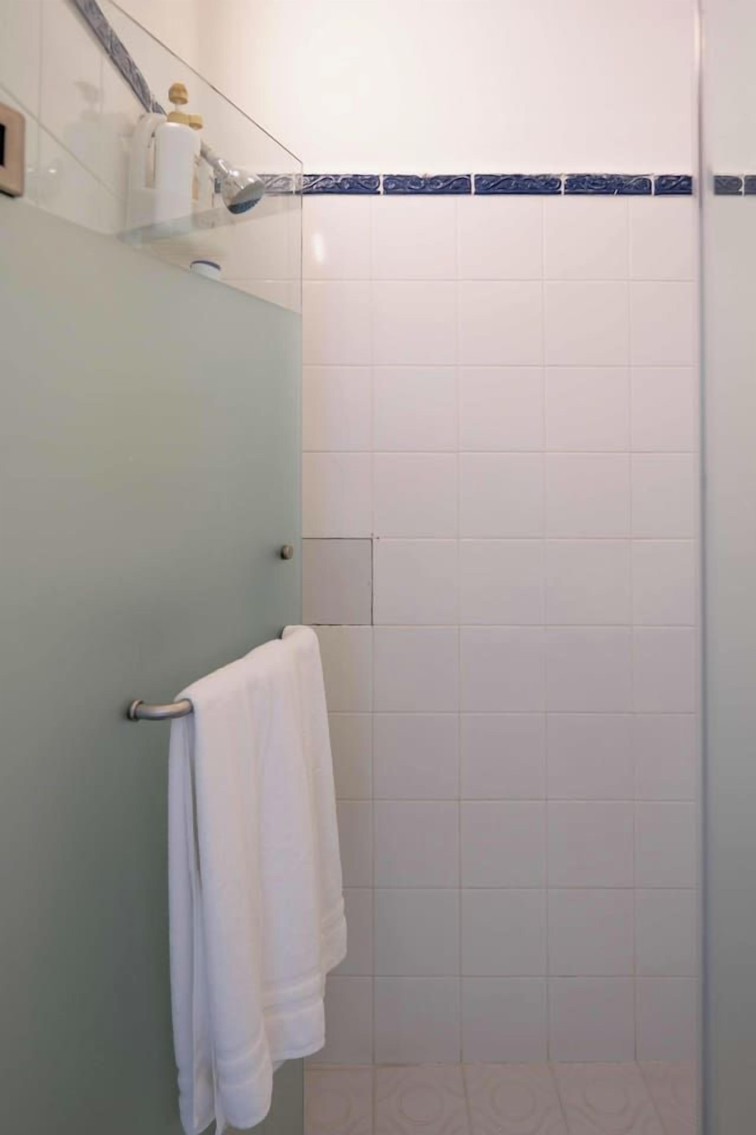 Een badkamer met een douchecabine van glas, een handdoekrek met een witte handdoek en een betegelde wand.