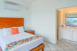 Une chambre d’hôtel comprenant un lit, une table de chevet, une salle de bain avec un lavabo et un miroir, et un appareil de climatisation fixé au mur.