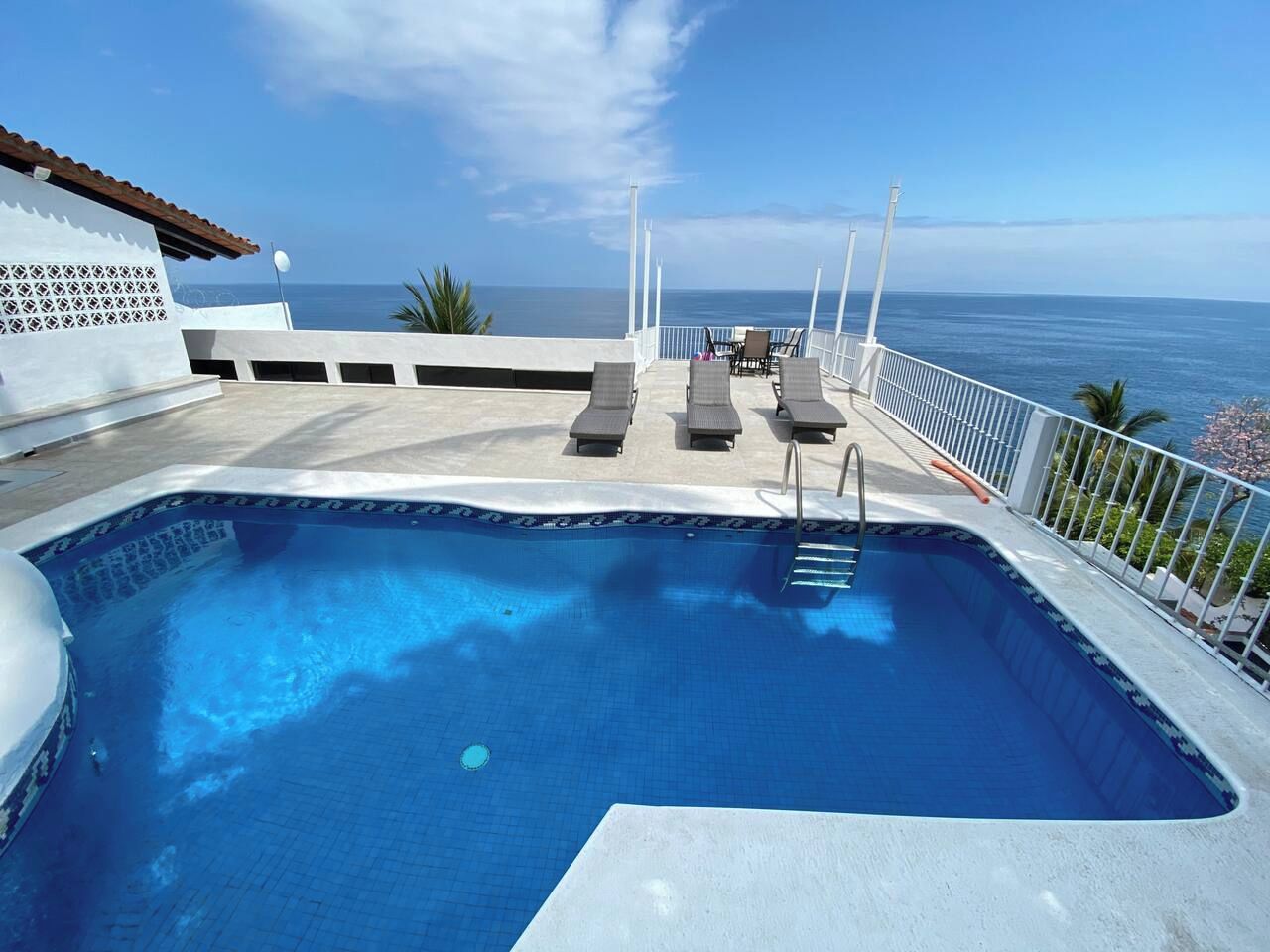 Piscina com espreguiçadeiras e vista para o oceano.