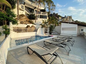 Un espace piscine comprenant des chaises longues, une petite piscine et un bâtiment doté de balcons.