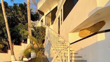 Un escalier menant à un bâtiment doté d’un balcon, entouré de palmiers et de rochers.