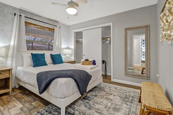 Un dormitorio moderno con cama, mesita de noche, silla, espejo y ventana con cortinas.