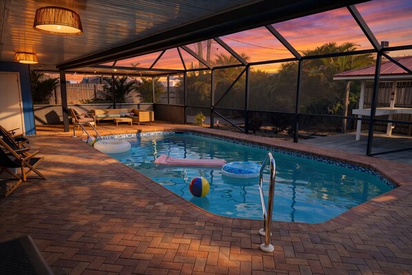 A swimming pool with a glass enclosure, lounge chairs, and a view of the sunset. - Modern Pool Home • Central Fort Myers Location (Fort Myers)