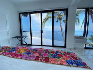 Een slaapkamer met een groot bed, een klein tafeltje en uitzicht op de oceaan door een schuifdeur.