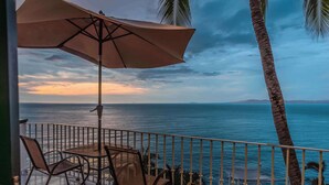 A balcony with a table and chairs, overlooking a coastal view with palm trees and a clear sky. - Condo 1 at Del Mar PV (Aguacate)