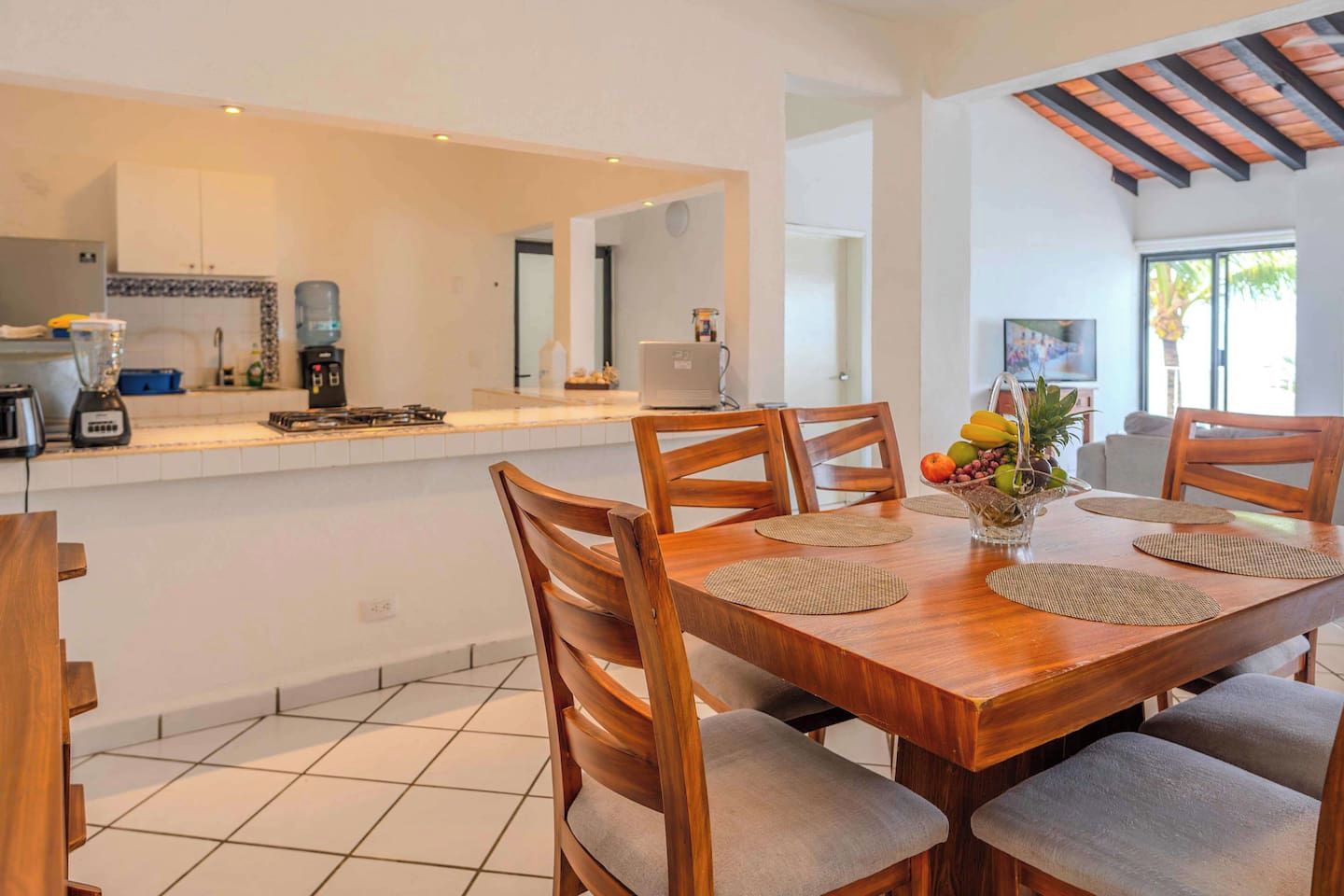 A modern kitchen with a central island, wooden dining table with chairs, and a view of the outdoors.