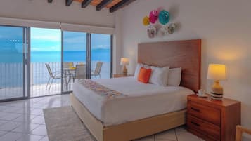 A hotel room with a large bed, a wooden headboard, a nightstand with a lamp, a small table with a cup, and a balcony with a table and chairs.