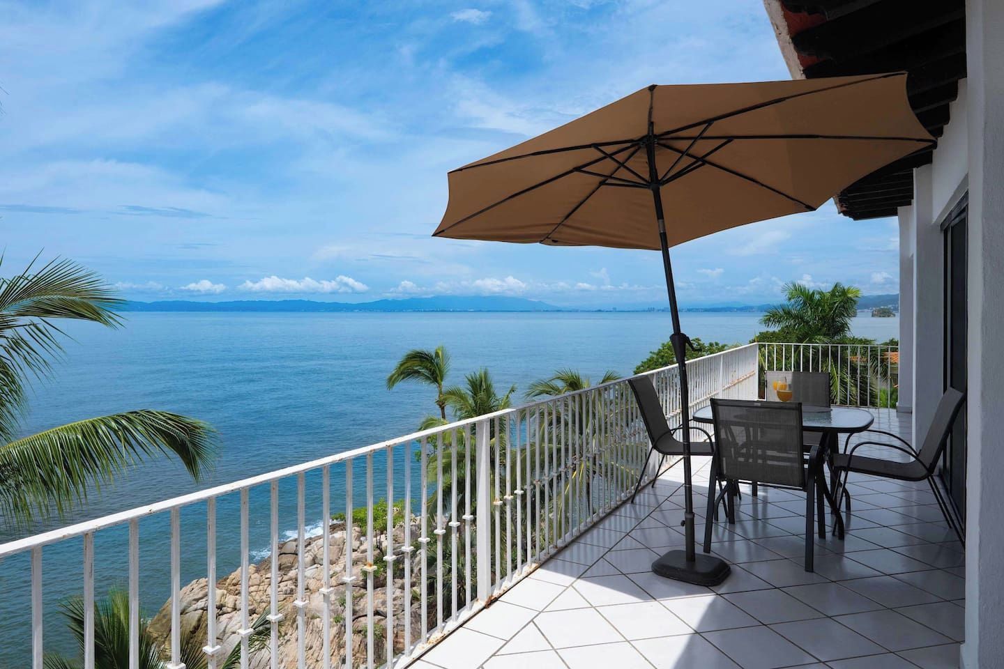 A balcony with a table and chairs, a large umbrella, and a view of the sea.