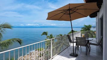 A balcony with a table and chairs, a large umbrella, and a view of the sea.