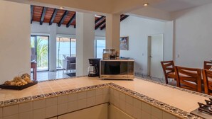 A spacious kitchen with a microwave, coffee maker, and a dining area with chairs. - Oceanfront Luxury Condo w/ Pool & Balcony Views (Aguacate)