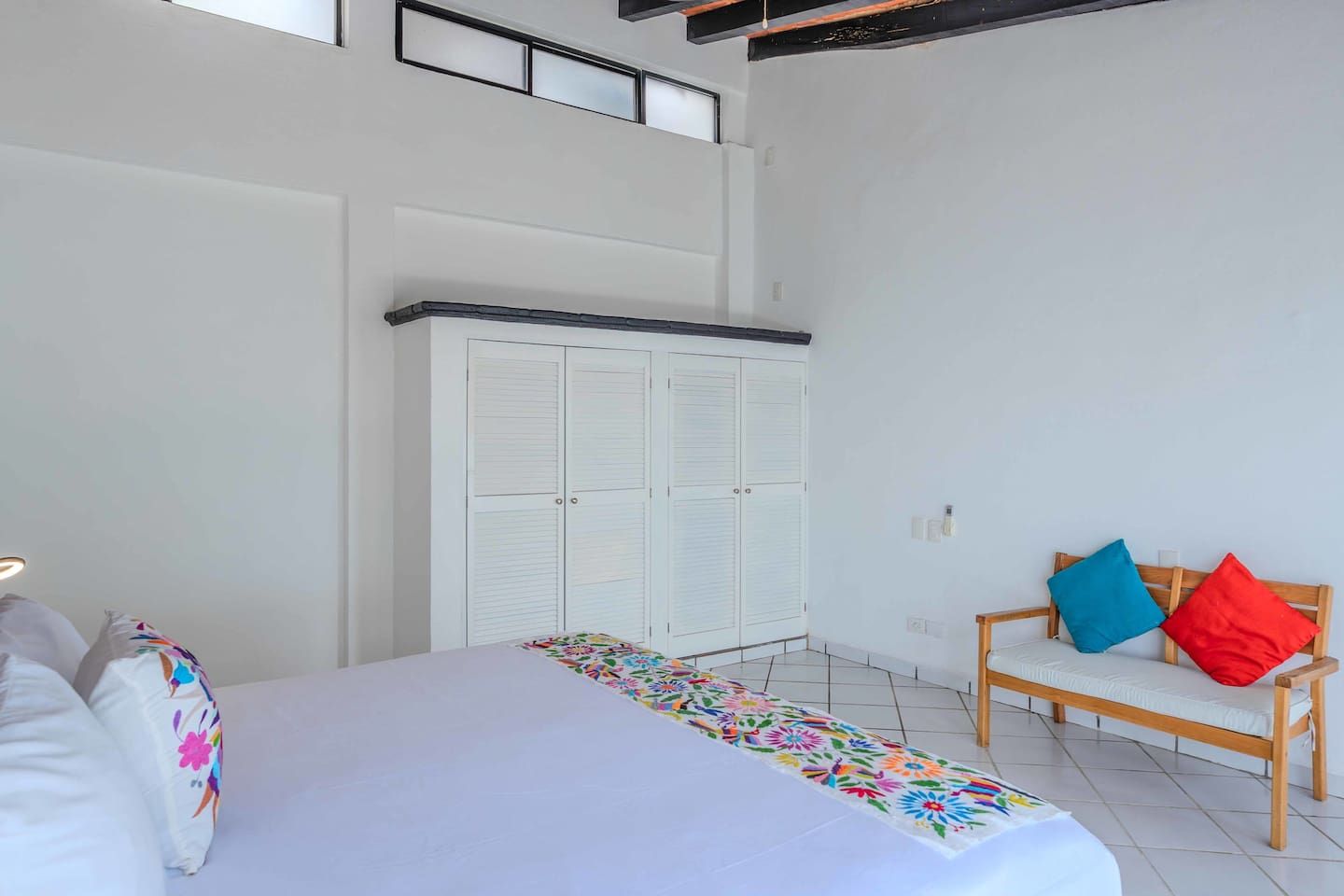 Ein Schlafzimmer mit einem Bett, einer Bank mit Kissen, einem Kleiderschrank und einem Fenster.