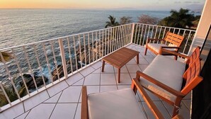 A balcony with a view of the ocean, featuring a wooden table and two wooden chairs. - Oceanfront Luxury Condo w/ Pool & Balcony Views (Aguacate)