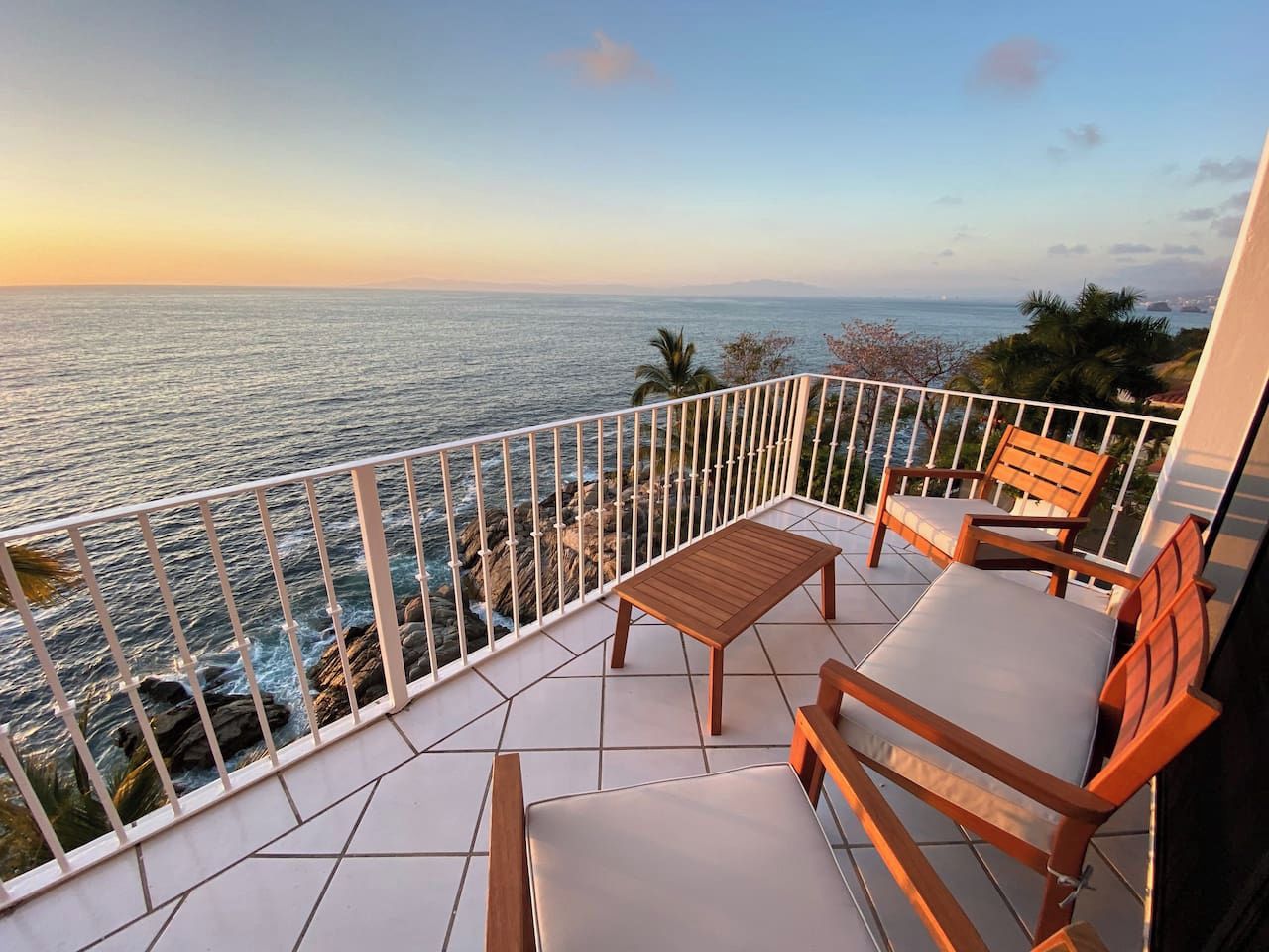 Un balcone con vista sul mare, un tavolo di legno e due sedie di legno.