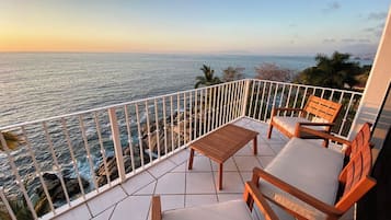 Un balcone con vista sul mare, un tavolo di legno e due sedie di legno.