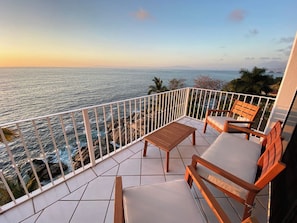 Un balcon avec vue sur la mer, une table en bois et deux chaises en bois.