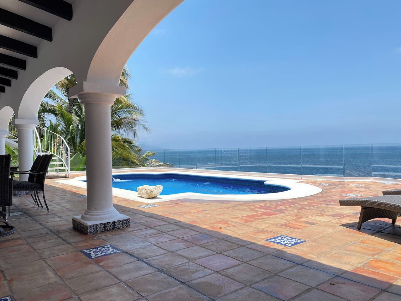 A pool area with a view of the ocean, outdoor seating, and a covered patio.
