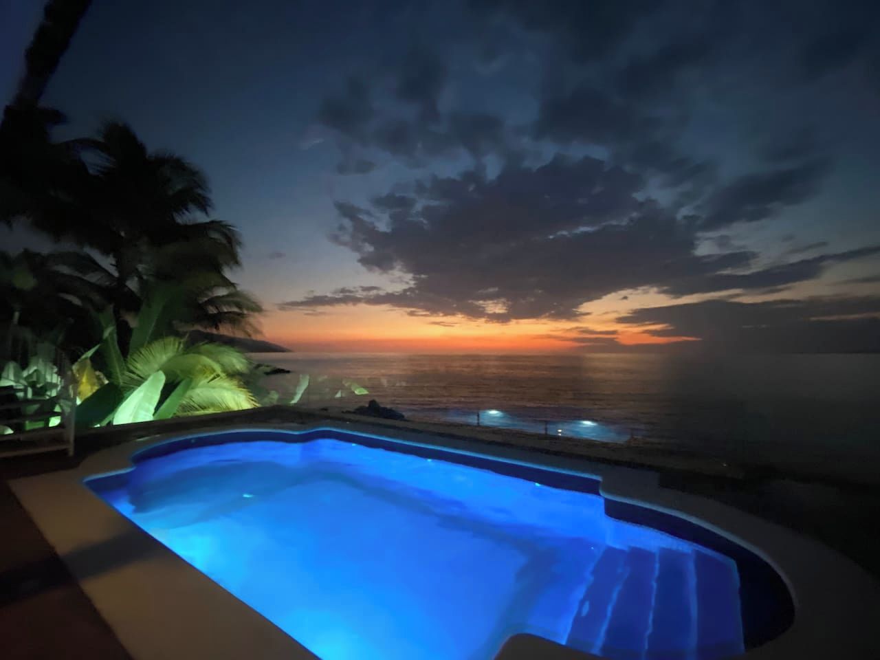 A swimming pool with a view of the ocean at sunset.