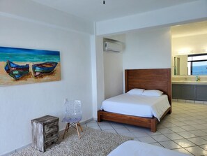 A bedroom with a bed, a painting of boats, a chair, and a small wooden cabinet. - Oceanfront Villa: Private Resort w/ Heated Pools (Aguacate)