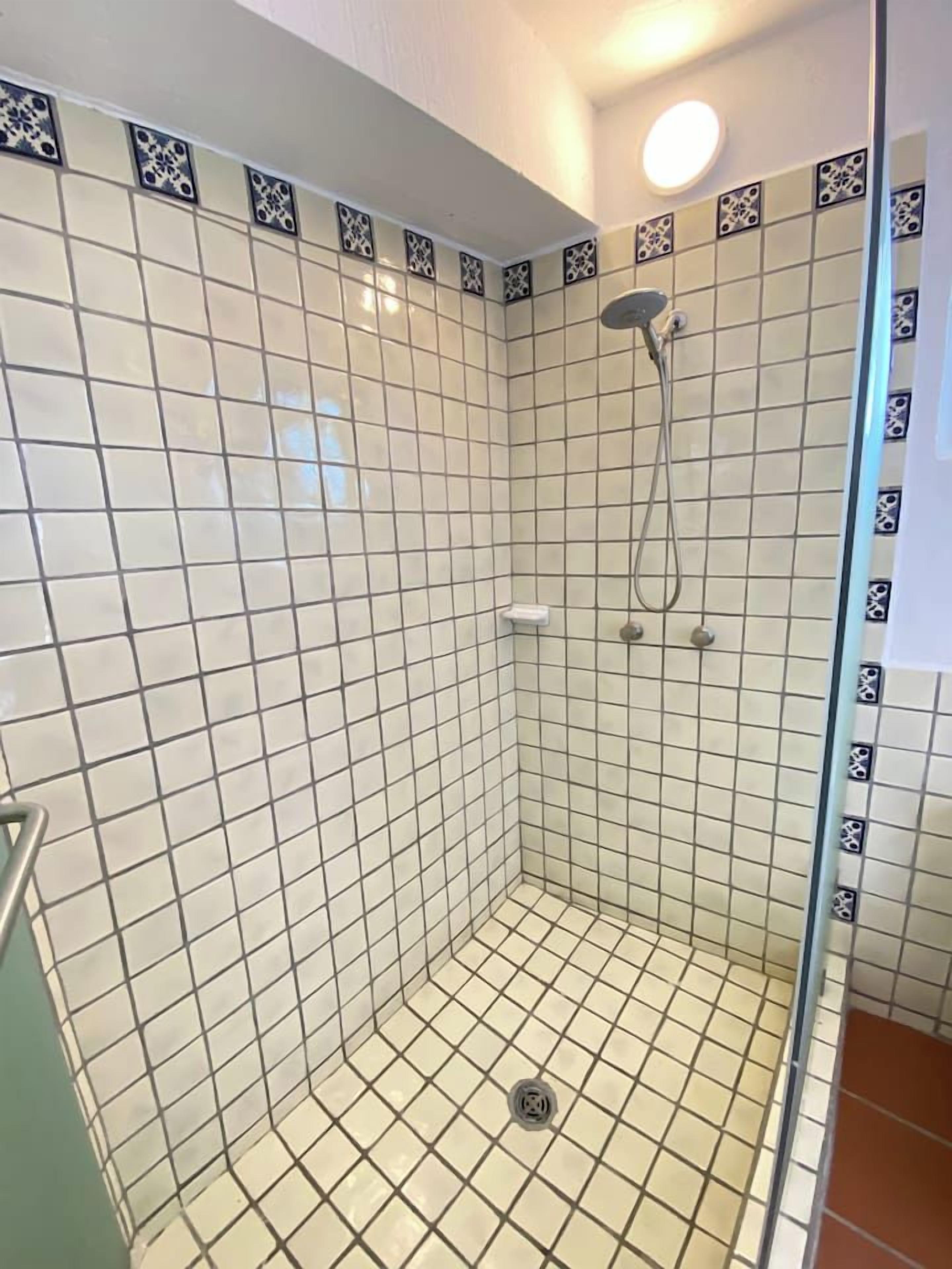 A tiled shower with a glass door, a showerhead, and a light fixture.