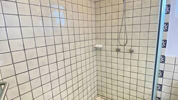 A tiled shower with a glass door, a showerhead, and a light fixture.