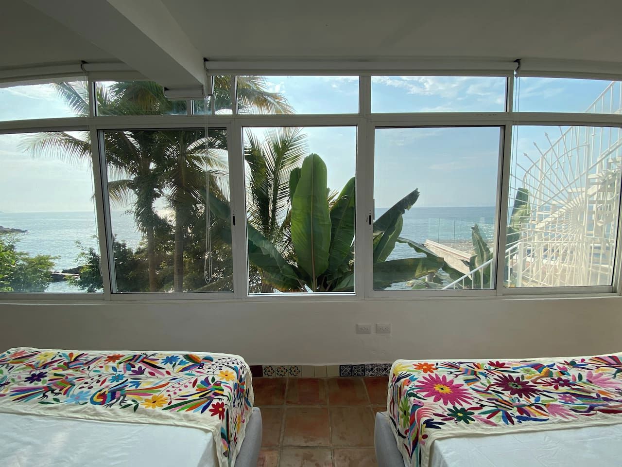 Una stanza con due letti, ampie finestre e vista sul mare e sulle palme.