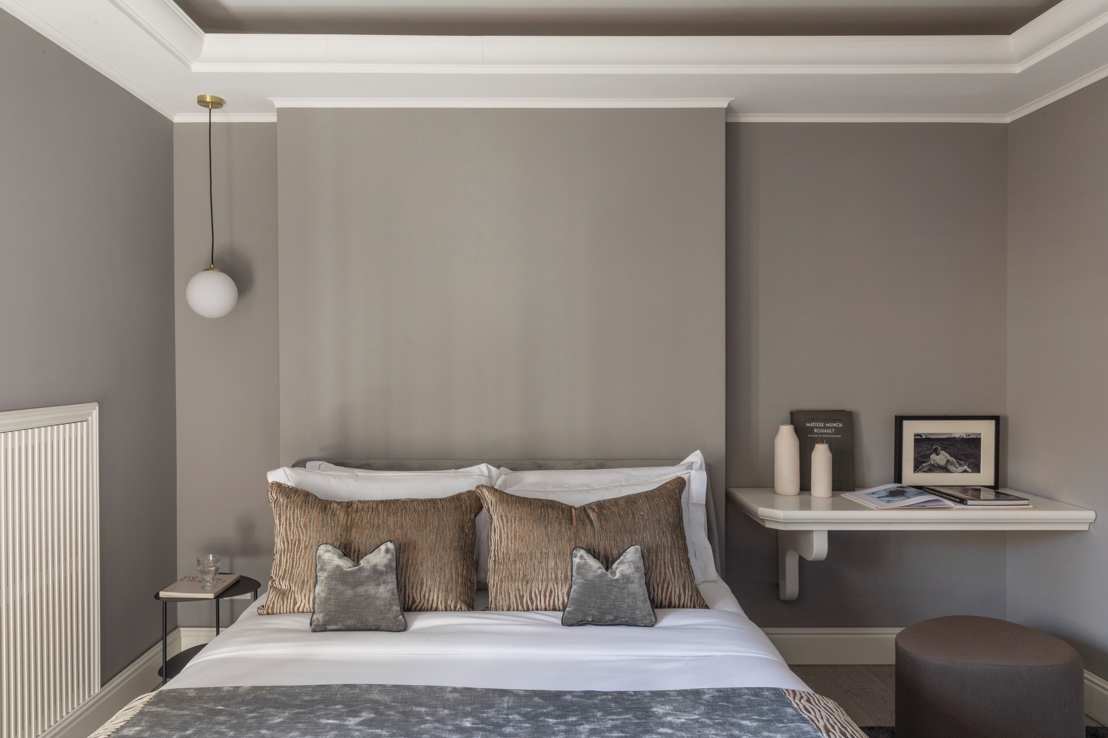 A neatly arranged bedroom with a bed, bedside tables, a shelf with books and decorative items, and a hanging light fixture.