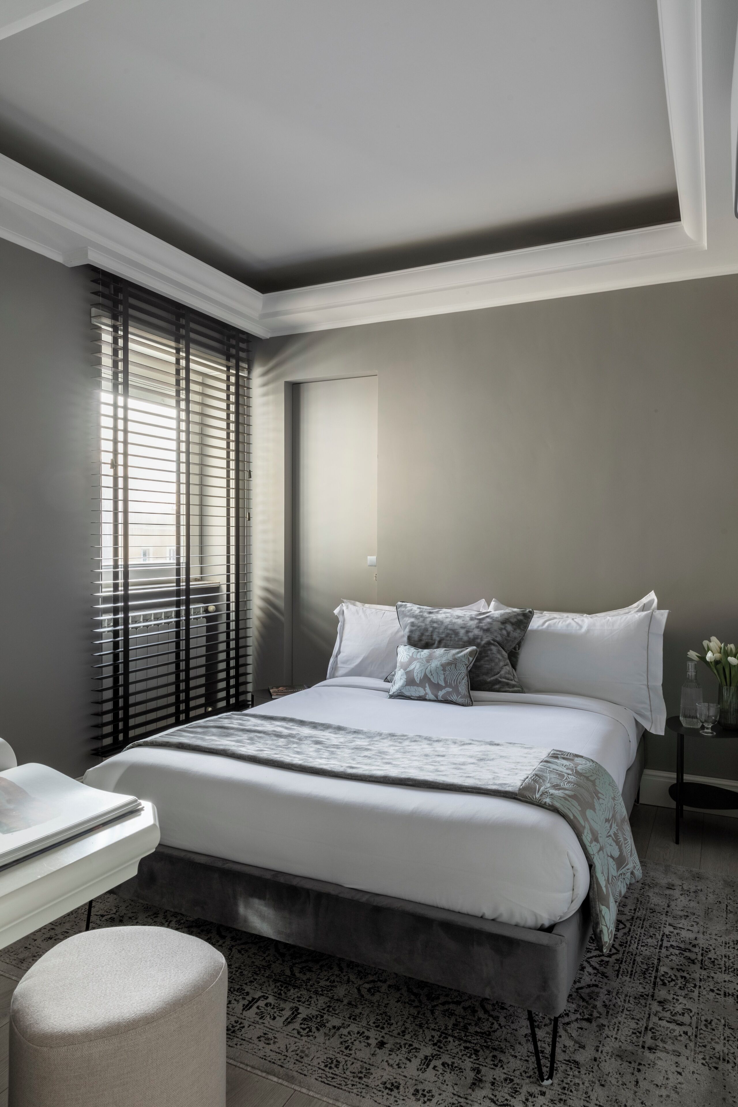 A modern bedroom with a large bed, a bedside table, and a window with blinds.