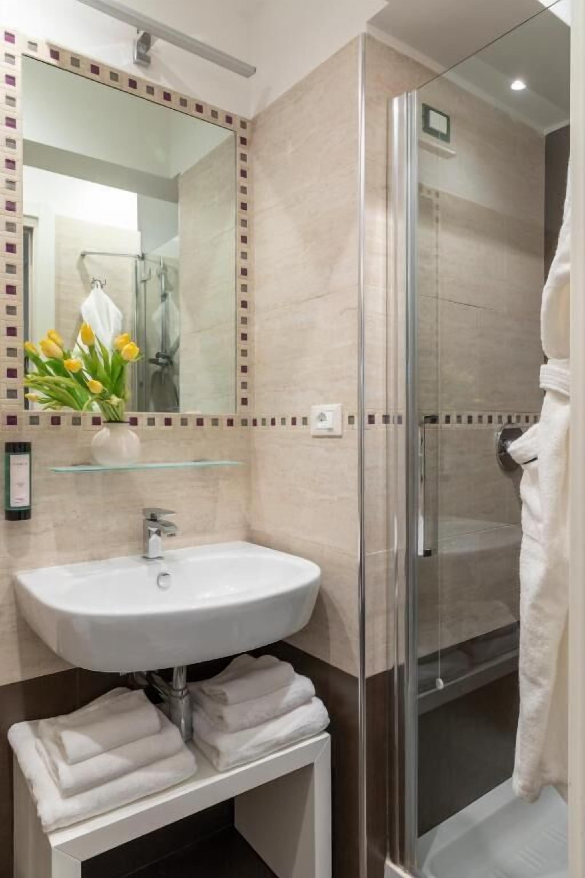 A modern bathroom with a glass-enclosed shower, a white sink, and a mirror with a decorative tile border.