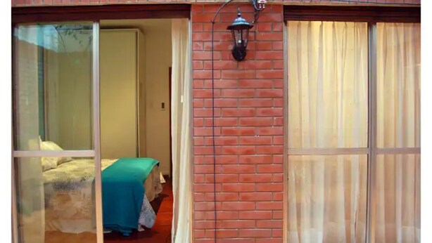 A room with a bed, a window with a curtain, and a brick wall.