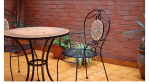 A patio with a round metal table and two chairs, a brick wall, and potted plants.