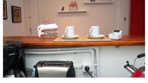 A kitchen counter with a coffee maker, toaster, and kettle. There are two white cups and saucers on the counter.