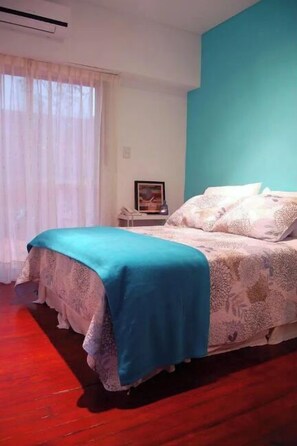 Quarto com cama, mesa de cabeceira e janela com cortinas.