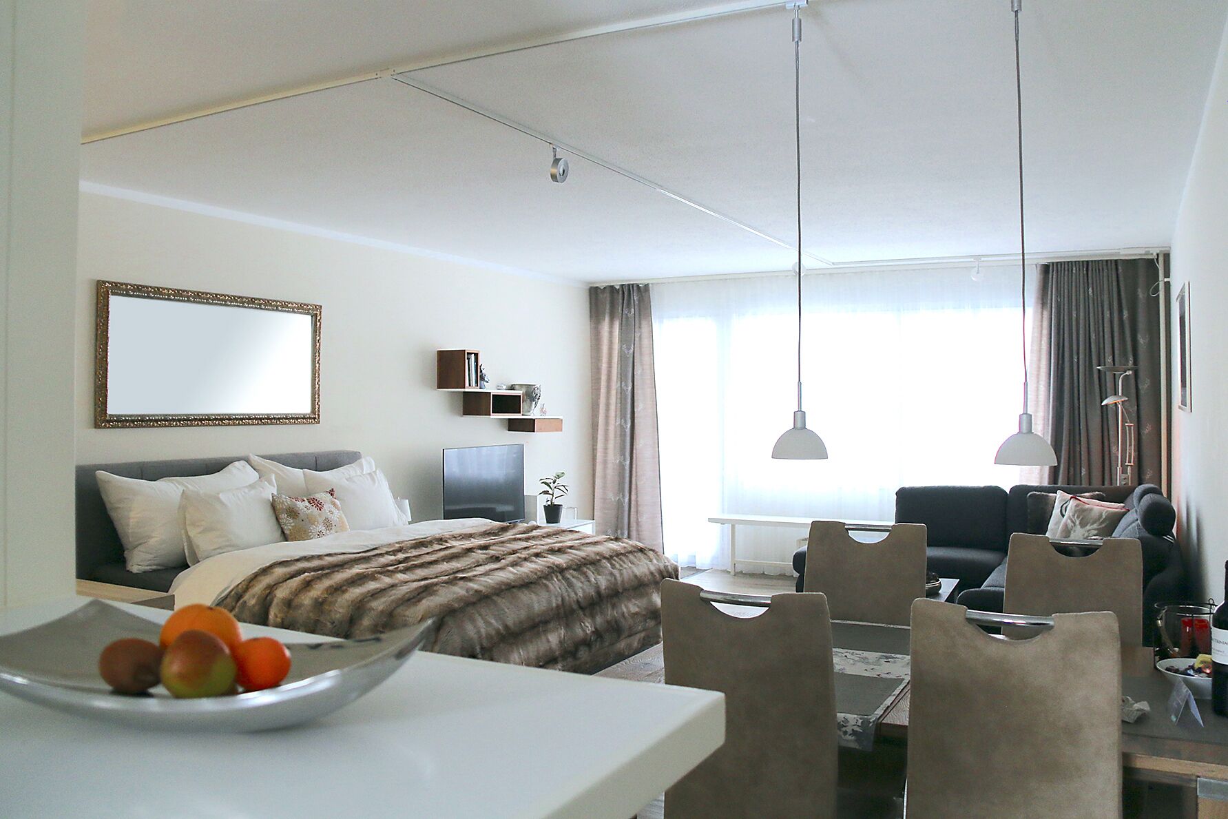 Una habitación de hotel moderna con una cama, un escritorio con un frutero, un televisor y un área de descanso con un sofá y sillas.