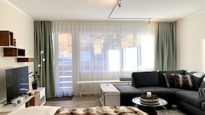 Moderni olohuone, jossa on sohva, taulutelevisio, ruokapöytä kakun kera ja pehmeä tekoturkispeitto.