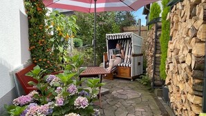 Un espace patio avec un sol en pierre, un parasol à rayures, une chaise et une personne qui lit un livre.