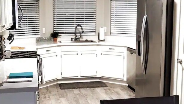 A modern kitchen with white cabinets, a stainless steel refrigerator, and a black chair. - Peoria Corner Lot 3 Bedroom 2 Bath with High Speed Internet/Smart TVs (Peoria)
