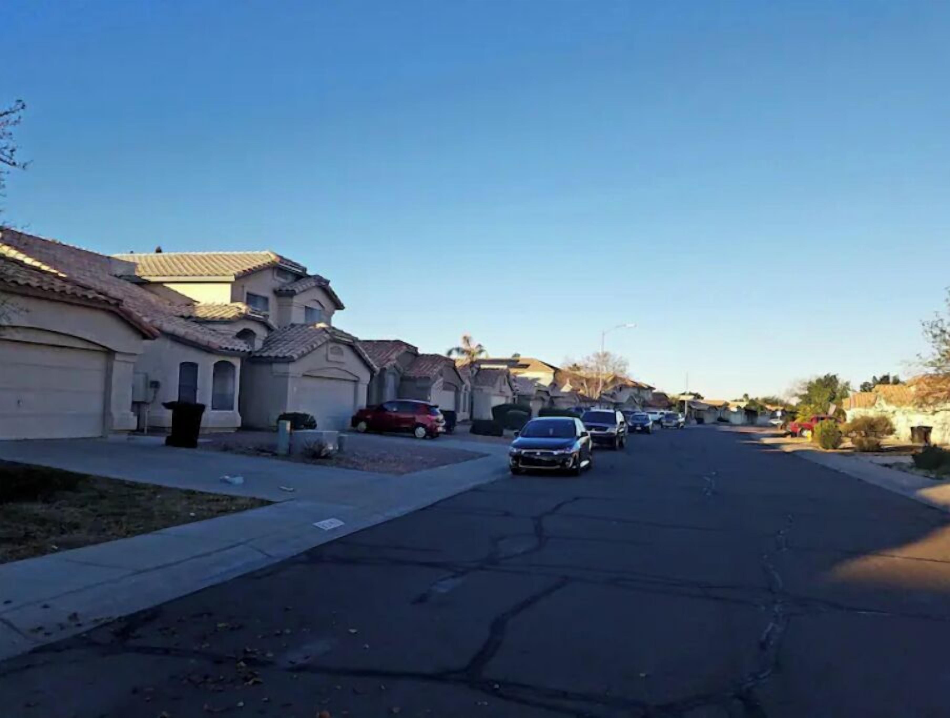 A residential street with houses, parked cars, and a clear sky.