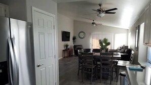 A modern kitchen with a refrigerator, a dining area with a table and chairs, a ceiling fan, and a clock on the wall. - Peoria Corner Lot 3 Bedroom 2 Bath with High Speed Internet/Smart TVs (Peoria)