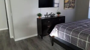 A bedroom with a bed, a dresser, a television mounted on the wall, and a small potted plant on the dresser. - Peoria Corner Lot 3 Bedroom 2 Bath with High Speed Internet/Smart TVs (Peoria)