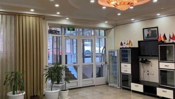 Een hotel lobby met glazen ingang, potplanten, een kroonluchter en een receptiebalie.
