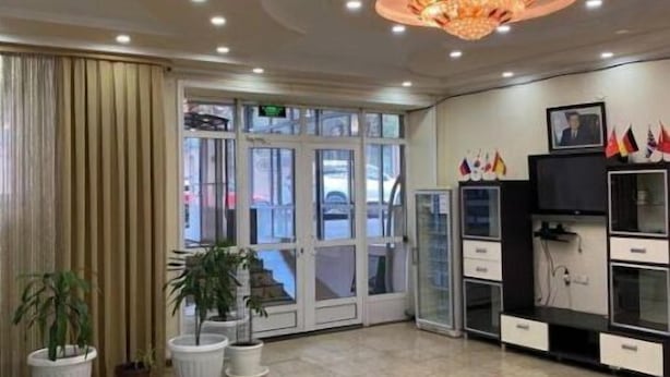 Un hall d’hôtel avec une entrée dotée d’une porte en verre, des plantes en pot, un lustre et un comptoir d’accueil.