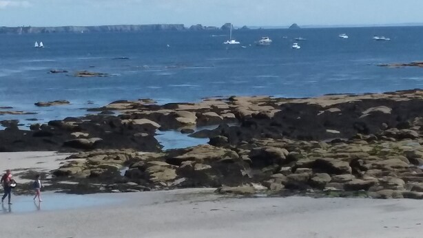 Una playa rocosa con barcos en el agua y un cielo despejado.