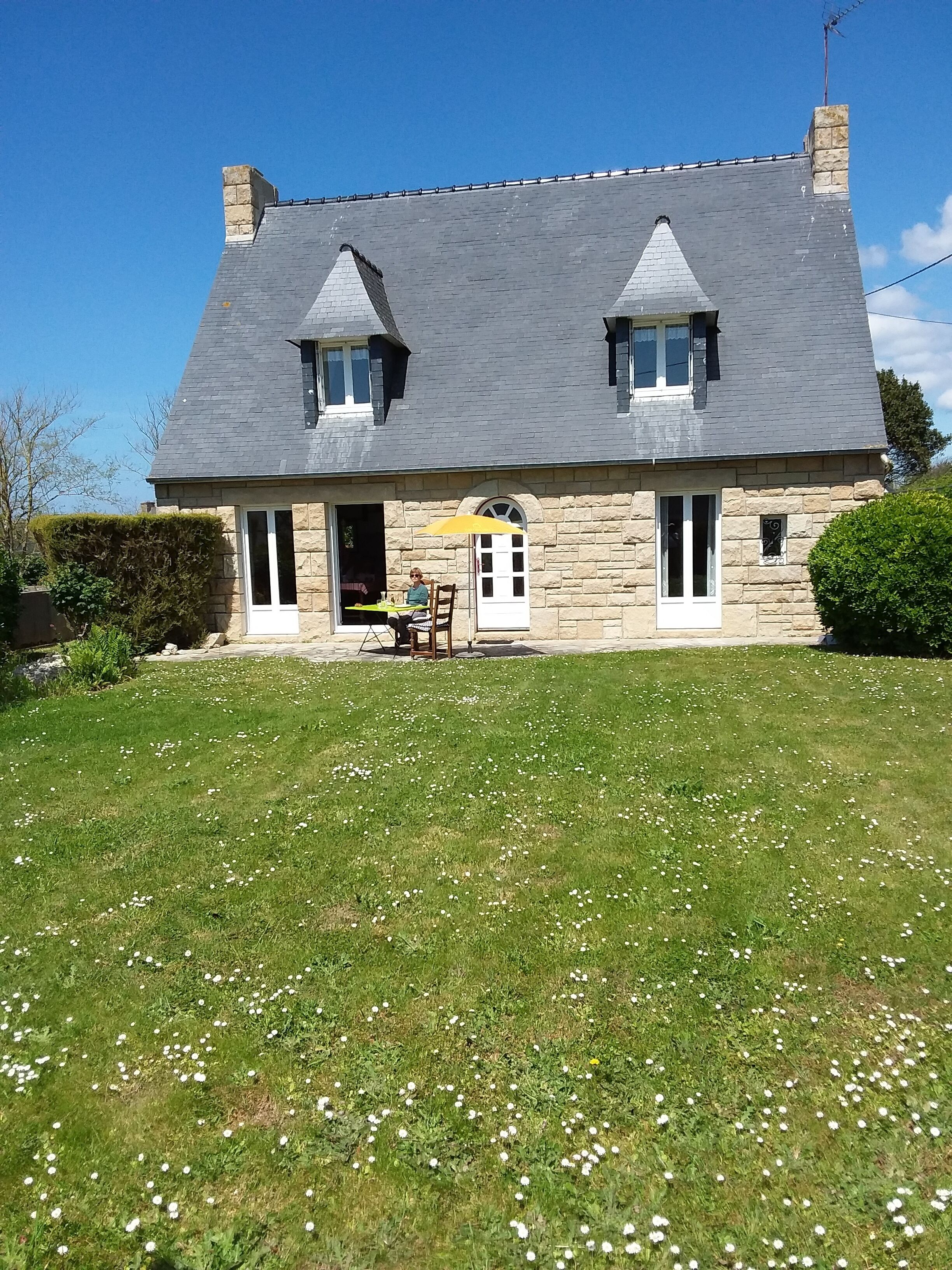 A stone house with a grey roof, two chimneys, and a small front porch.