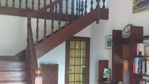 Una escalera de madera con barandilla conduce a una plataforma. Se ve una estantería con libros y un plato decorativo en la plataforma.